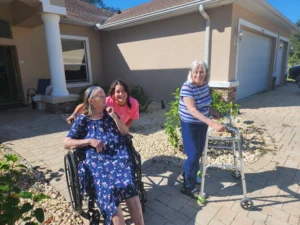 Two elderly women with mobility aids and a younger woman smiling outside a house.