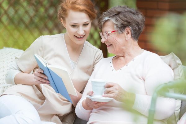 Beautiful redhead nurse reads a book to elderly lady in the garden